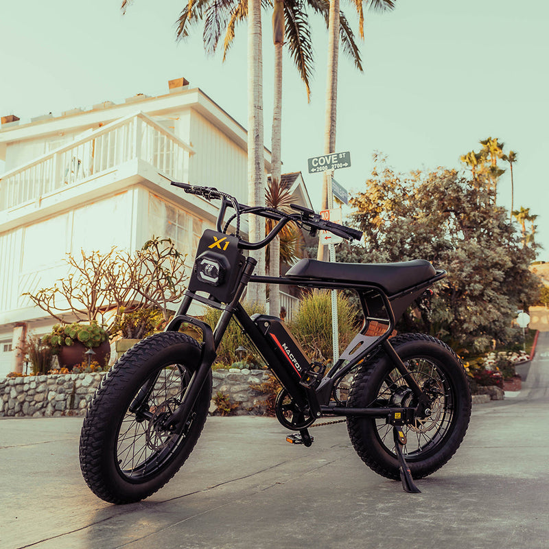Macfox X1S electric bike parked in front of a modern beachside home, showcasing its rugged frame, fat tires, and urban styling at sunset.