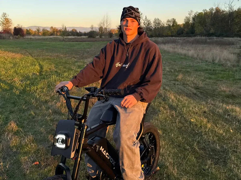 Rider holding a Macfox X2 full-suspension e-bike in a wide open field at sunset