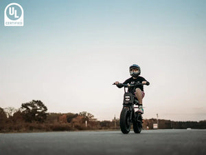 The little boy is riding a Macfox M16 electric bicycle on the street, wearing a helmet.