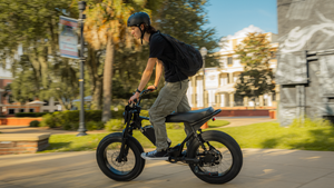 A helmeted rider riding a black Macfox X2 Pro electric bike through a neighborhood.
