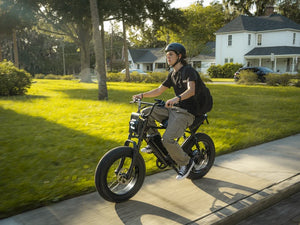 A helmeted rider riding a black Macfox X2 Pro electric bike through a neighborhood.