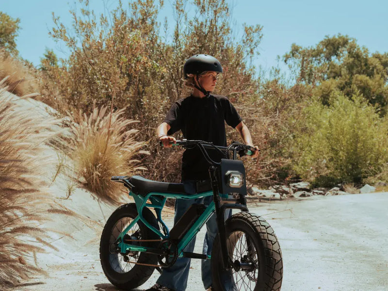 younger rider on a Macfox X7 ebike stopped on a paved path near plants and trees