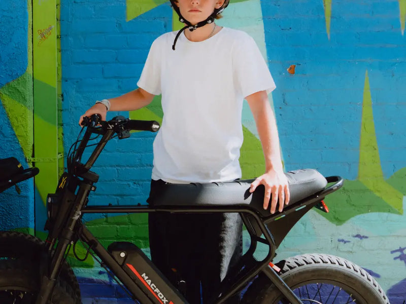 Rider standing beside a Macfox X1S commuter e-bike against a colorful urban wal