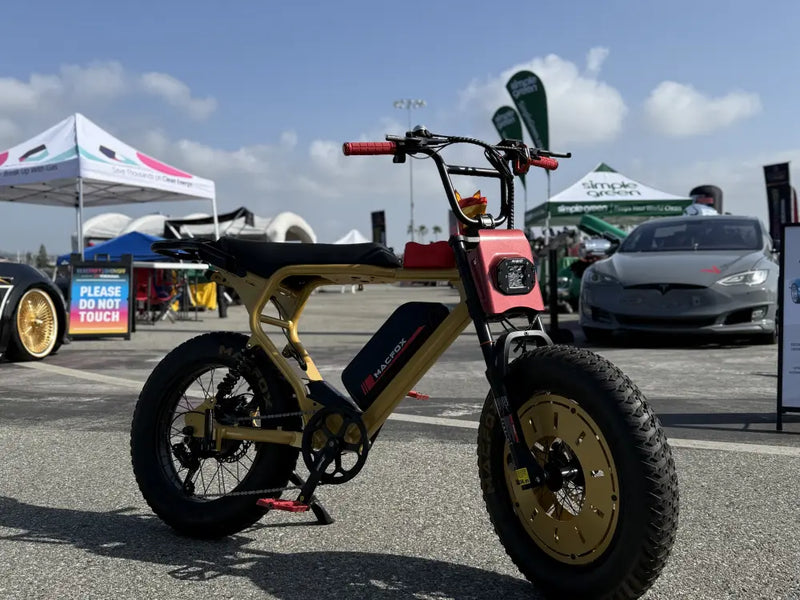 Macfox X2 ebike parked outdoors at an event area with tents and vehicles behind