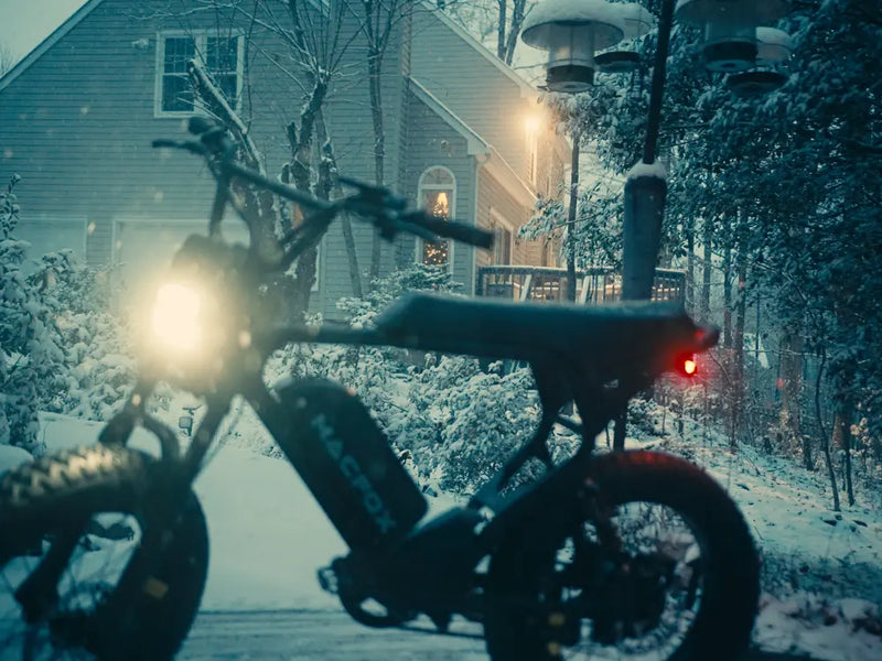 Macfox X7 fat-tire e-bike parked outdoors during winter conditions, with lights on in a snowy setting