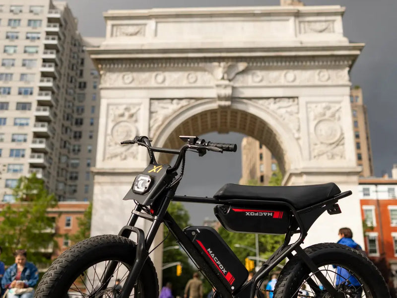 Macfox X1S electric bike parked near an urban landmark arch