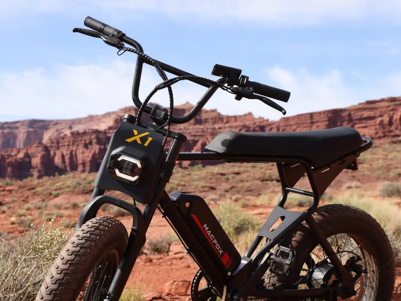 Macfox X1S commuter e-bike parked on a rocky hillside trail, showing fat tires and sturdy frame