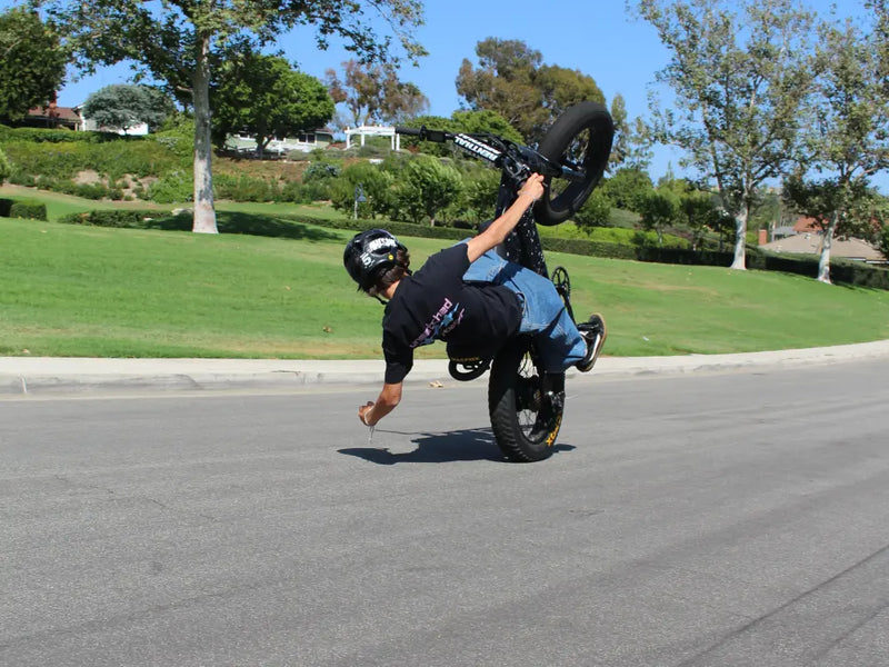 younger rider performing a wheelie on a Macfox X1S ebike on a paved road