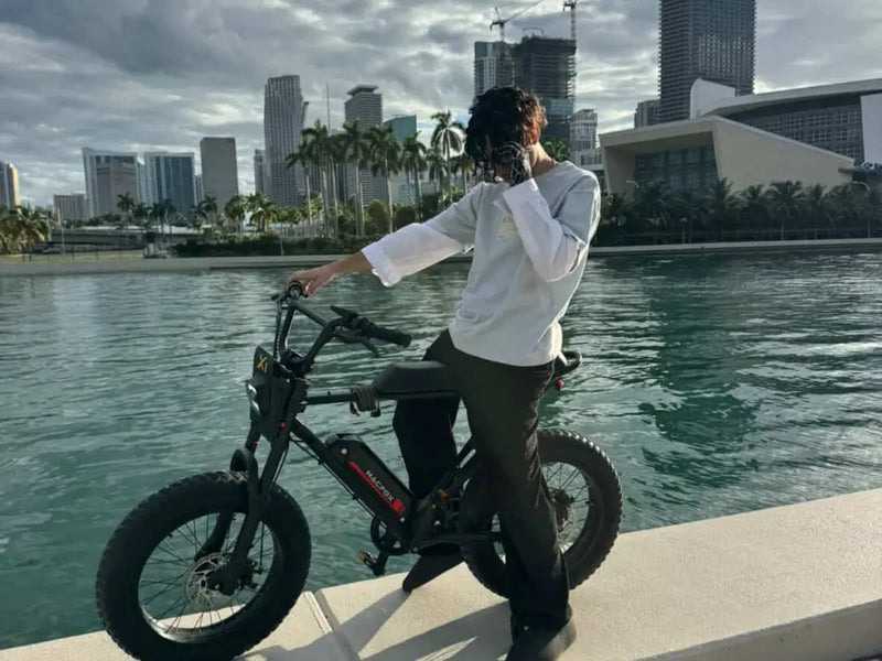 Macfox X1S electric bike parked beside the water with city skyline in background