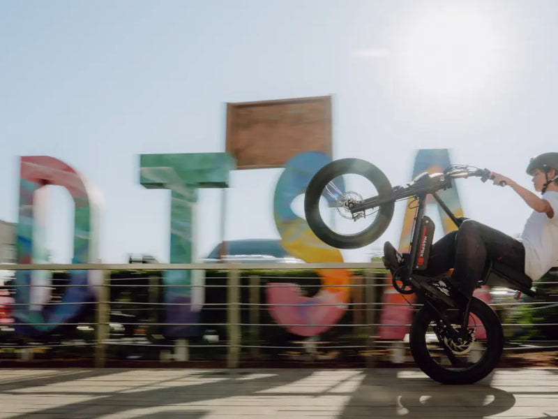 Rider performing a wheelie on a Macfox X1S eBike in front of colorful outdoor art