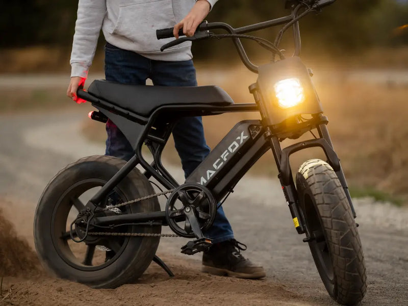 Rider riding a Macfox M16 electric bike on a dirt path with headlight on