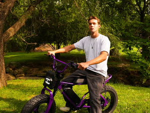 A person seated on a stationary purple Macfox X7 eBike beneath a tree.