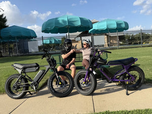 Two people seated on a park bench with Macfox electric bikes parked in front.
