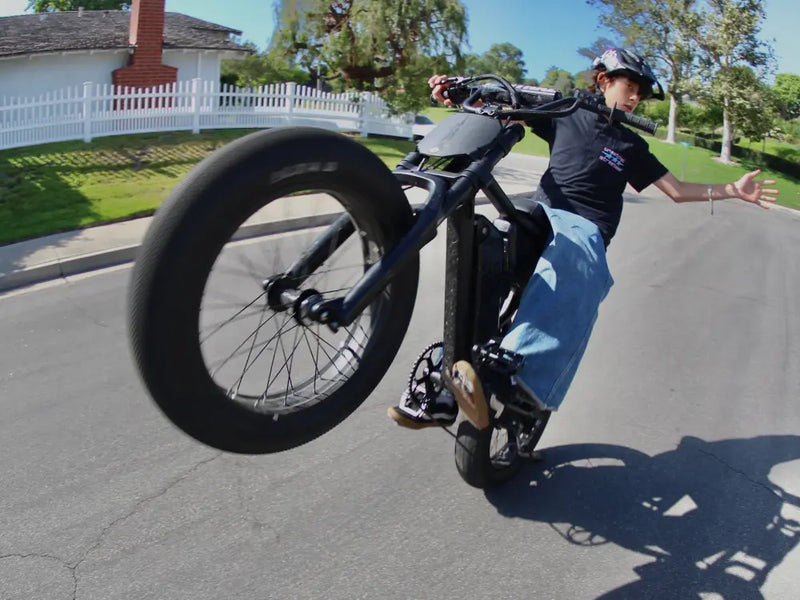 Rider performing a wheelie on a Macfox X1S electric bike on a sunny street