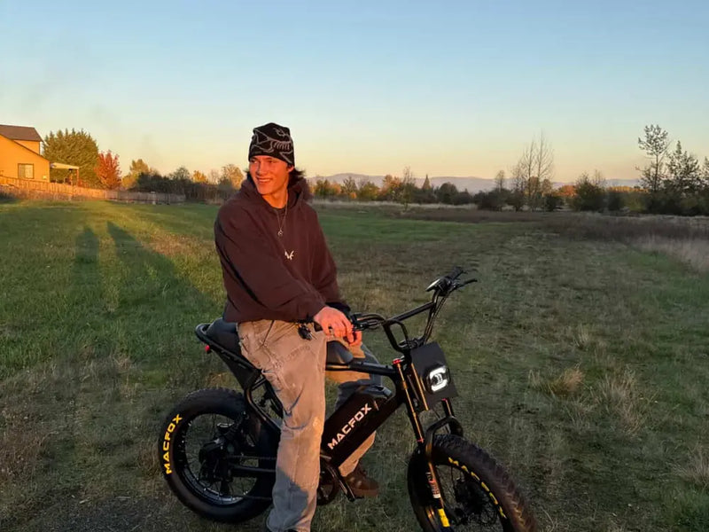 younger rider sitting on a Macfox X2 ebike in an open grassy field at sunset