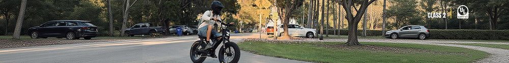 A helmeted rider cruises along a tree-lined residential street on a Macfox X7 fat tire electric bike.